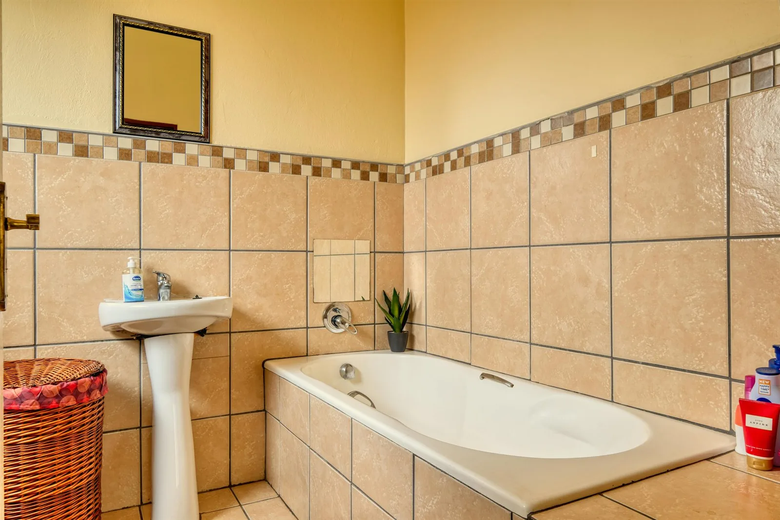 Warm tiled bathroom with one compact plant placed near the bathtub
