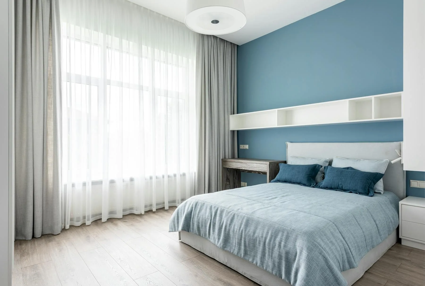 Blue bedroom with pale floor, sheer curtains, and soft bedding
