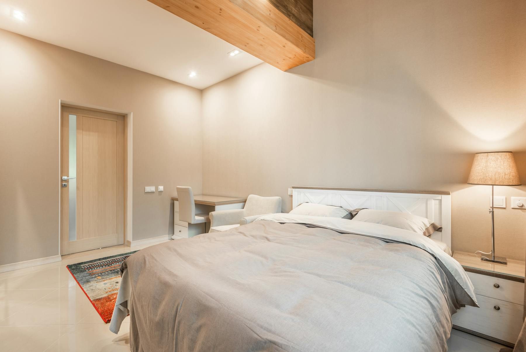 Neutral bedroom with the bed on a solid wall and a calm open pathway toward the door
