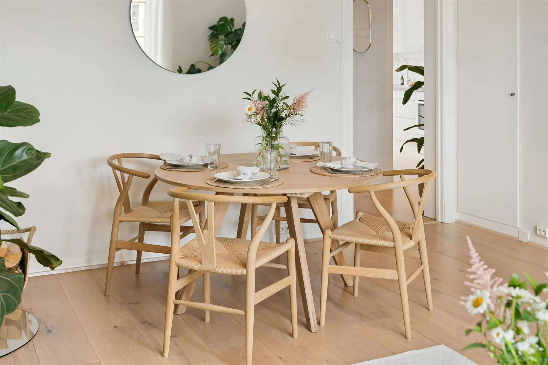 Round light-wood dining table with balanced chairs, flowers, and open circulation around the room