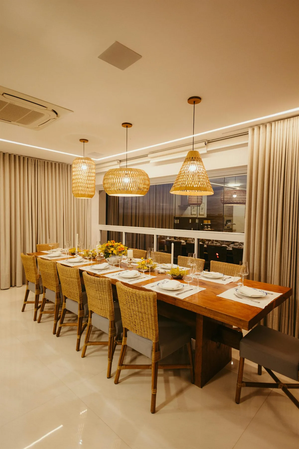 Long wood dining table with woven chairs and warm pendant lights