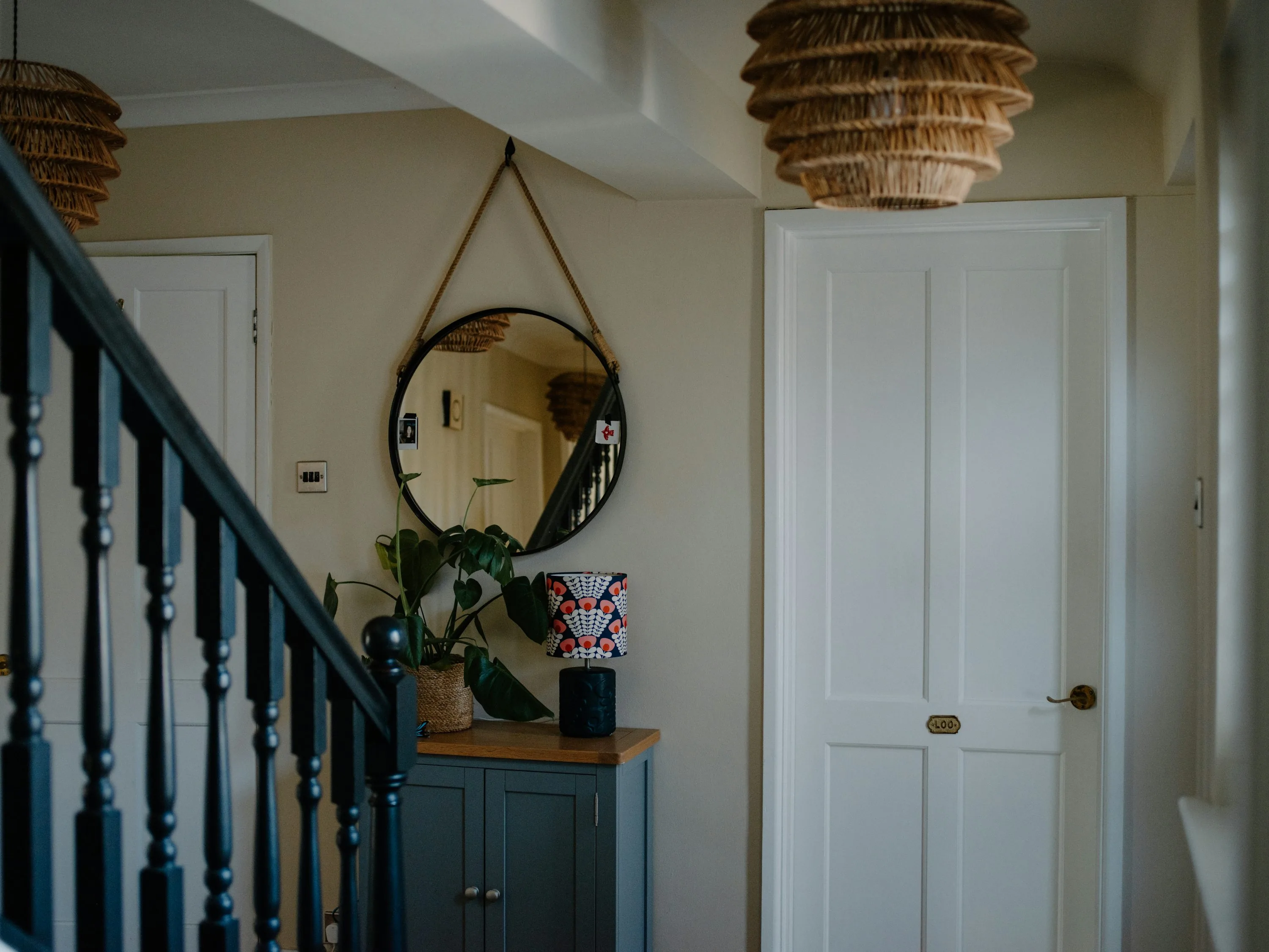 Entryway with muted blue-gray cabinet, warm wall tone, round mirror, and nearby stair rail