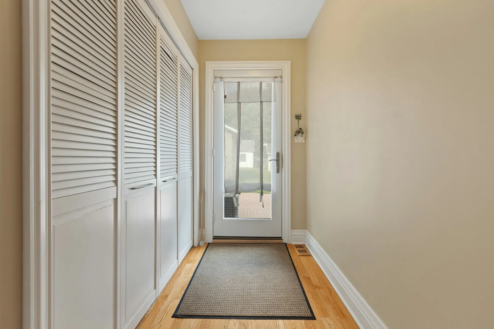 Narrow entry hall with warm beige walls, white closet doors, a gray runner, and daylight at the far door