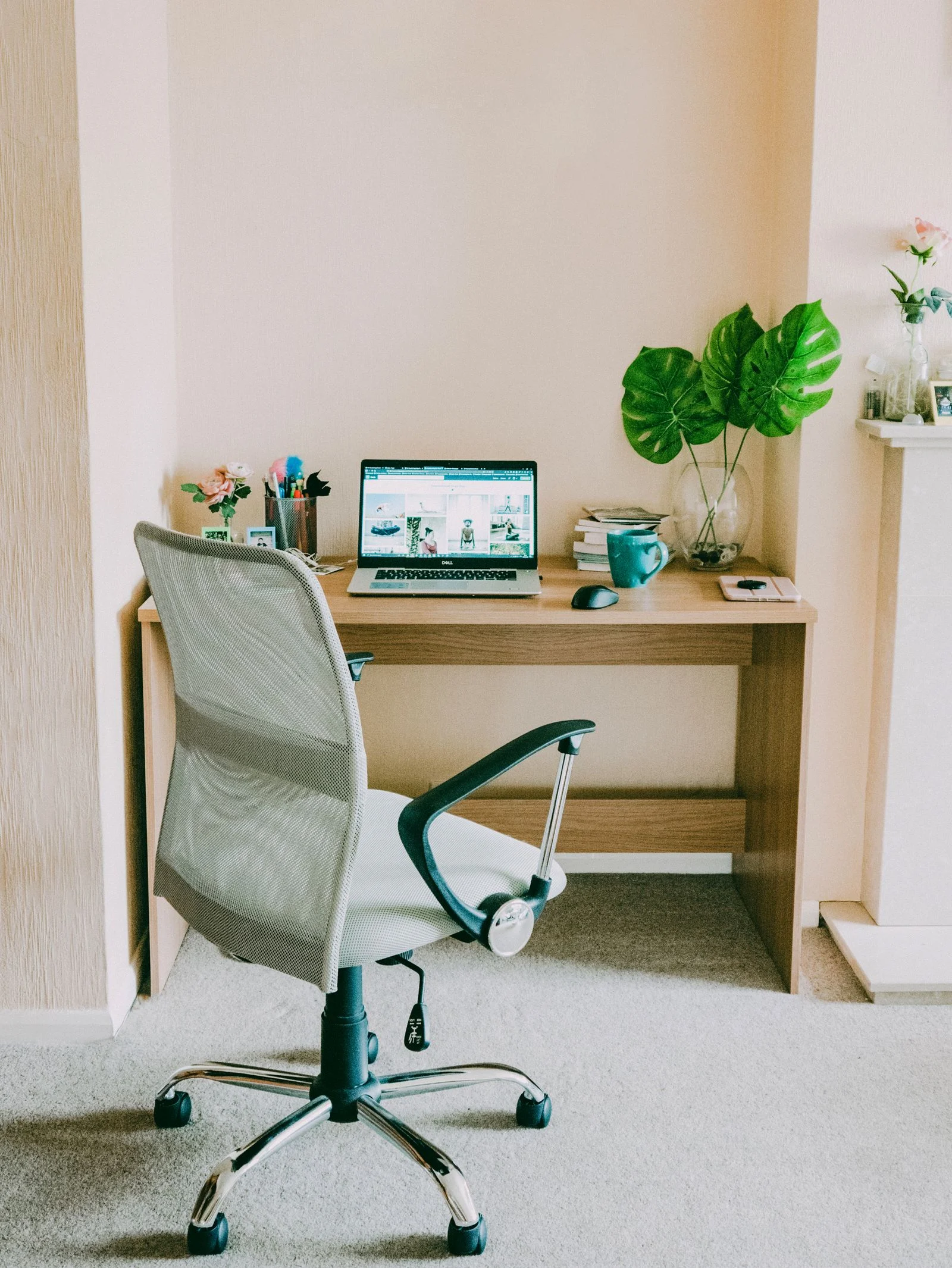 A laptop on a compact wooden wall-facing desk with an adjustable office chair
