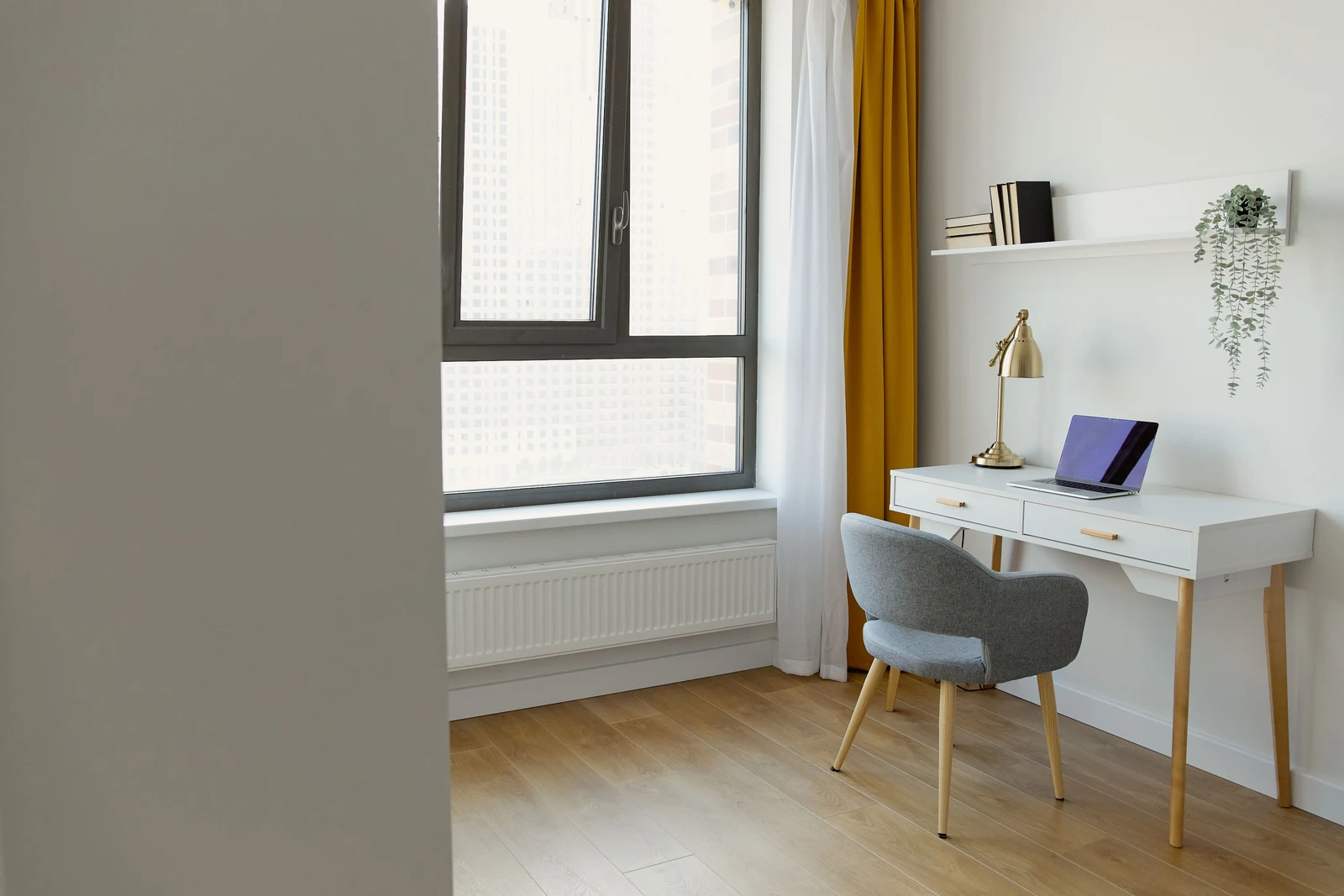 A compact wall-facing desk beside a window with space around the chair