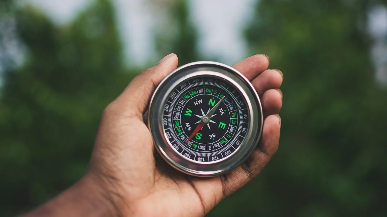 A hand holding an analog compass with a visible directional scale