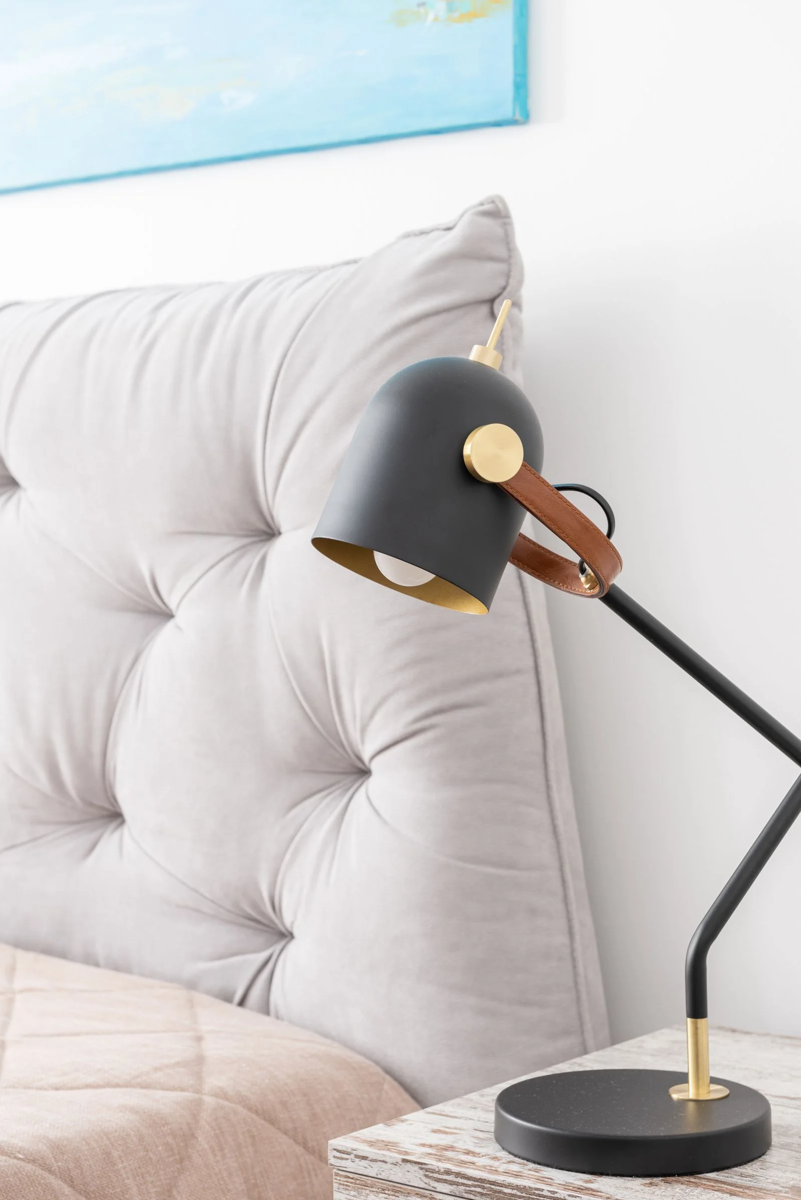Adjustable black bedside lamp with a gold-lined shade next to a tufted pale headboard