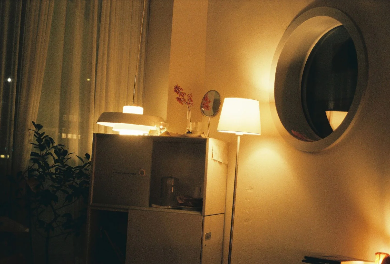 Warm floor lamp beside a cabinet, pendant lights and a round mirror in an evening interior