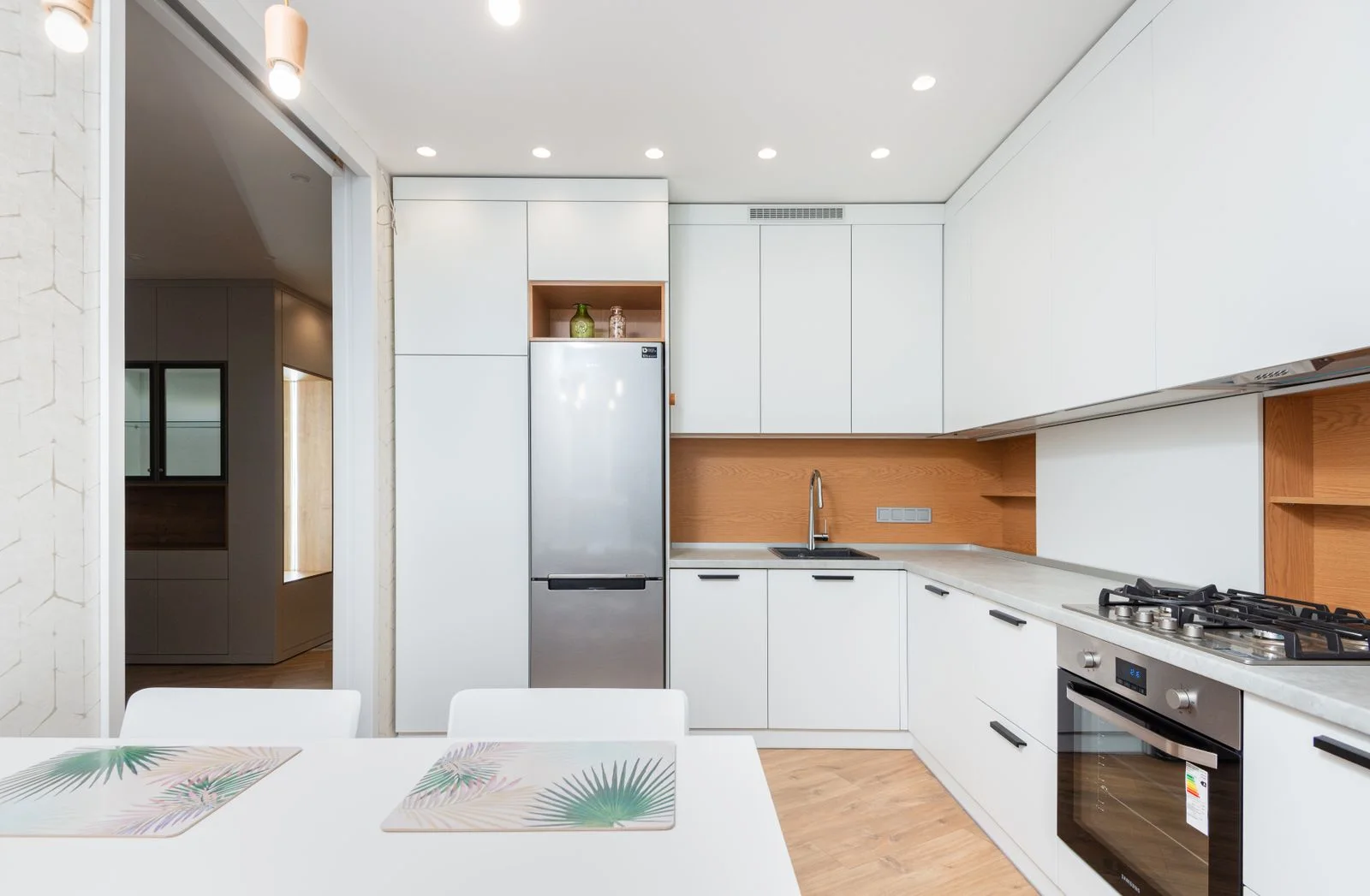 White kitchen with recessed ceiling lights, small pendants above a table and light beneath upper cabinets
