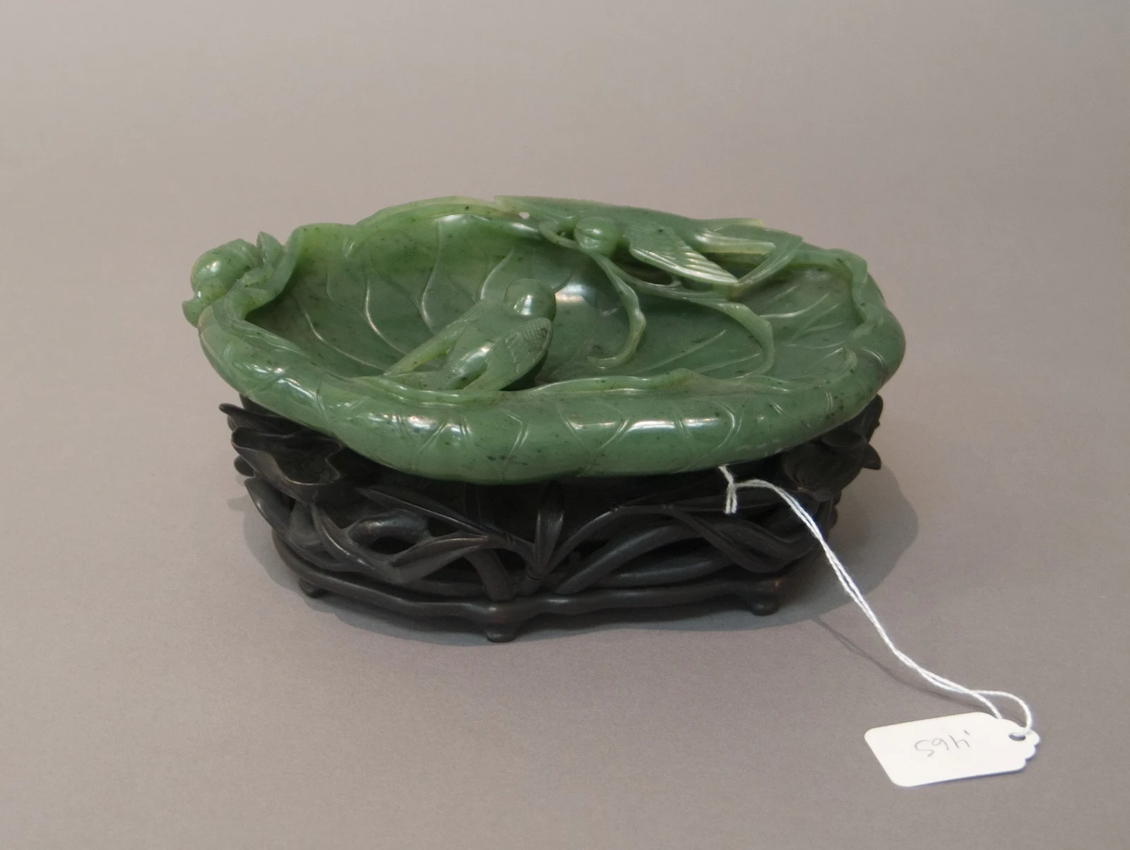 An olive-green nephrite dish carved as a lotus leaf with raised veins, displayed on a dark stand