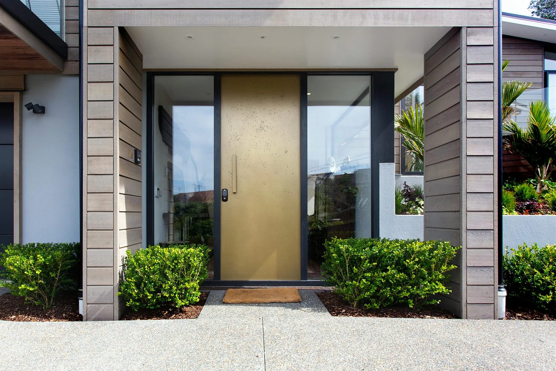 Warm tan front door framed by dark trim on a modern exterior with wood siding