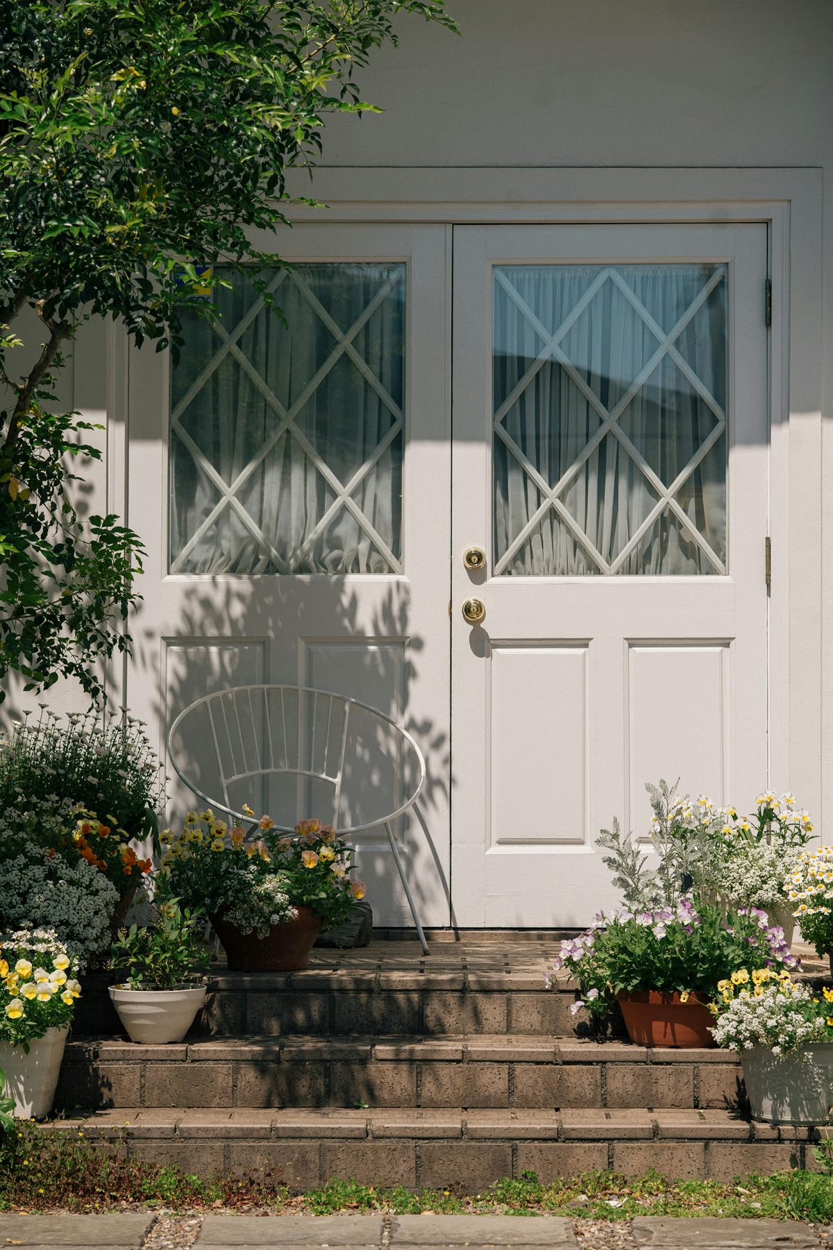White front door with flowers arranged along the steps and a soft light exterior wall