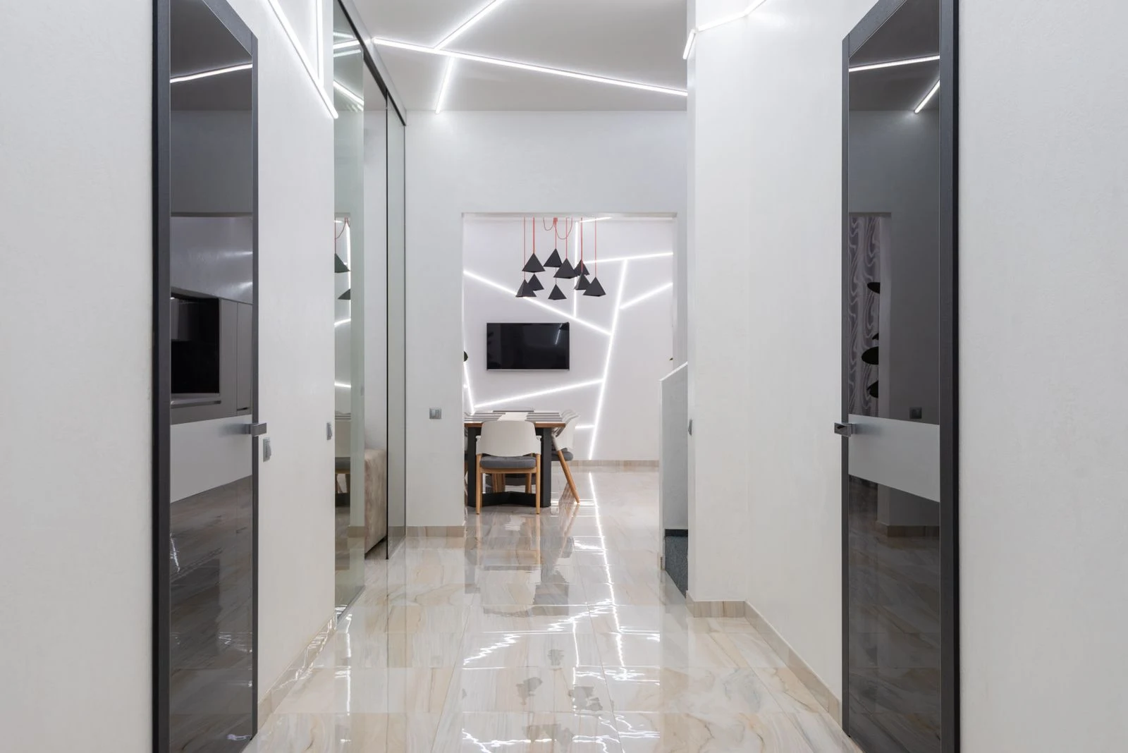White apartment hallway with geometric ceiling lights, dark glazed doors and a clear tiled floor