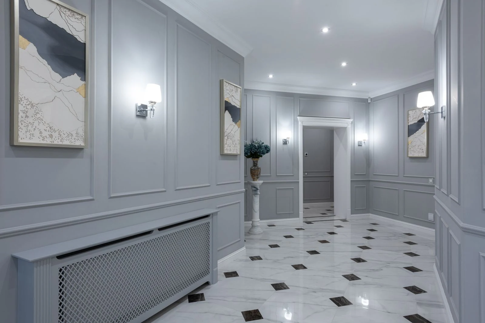 Gray paneled hallway with coordinated abstract paintings, wall sconces and a radiator cover along one wall