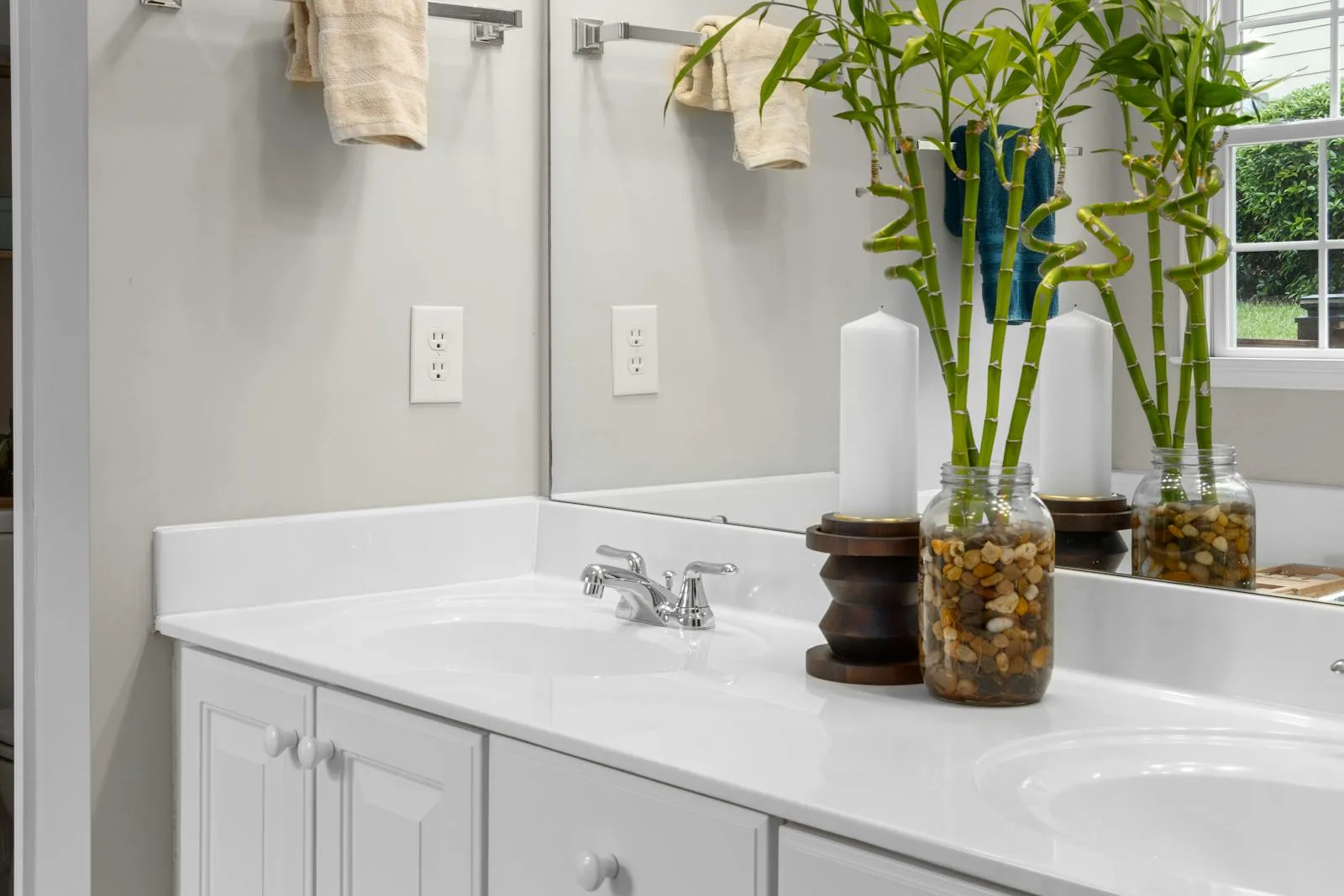 Bathroom vanity with tall bamboo-style plants and a clear double sink counter