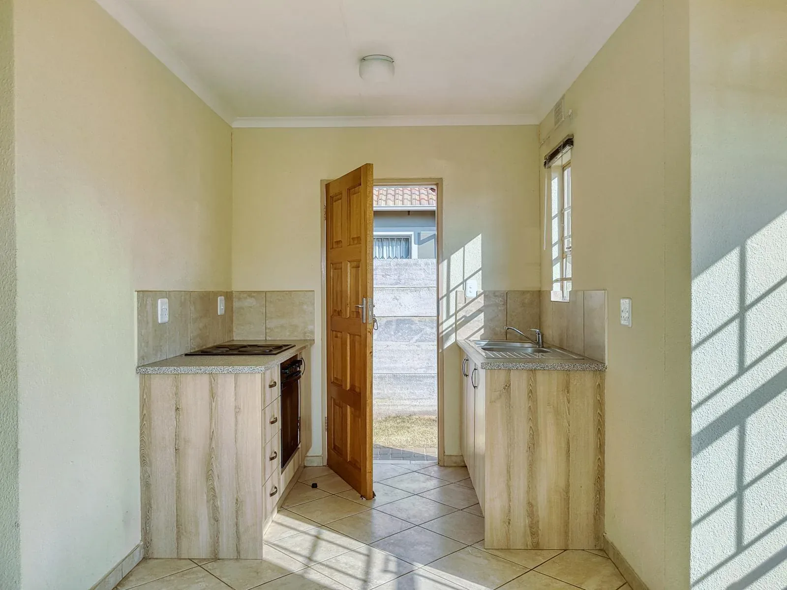 Sunlit kitchen with pale green walls, warm wood door, and a softer nourishing palette