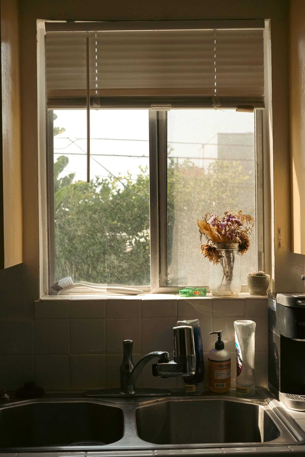 Kitchen sink below a window with warm late light and a small vase on the sill