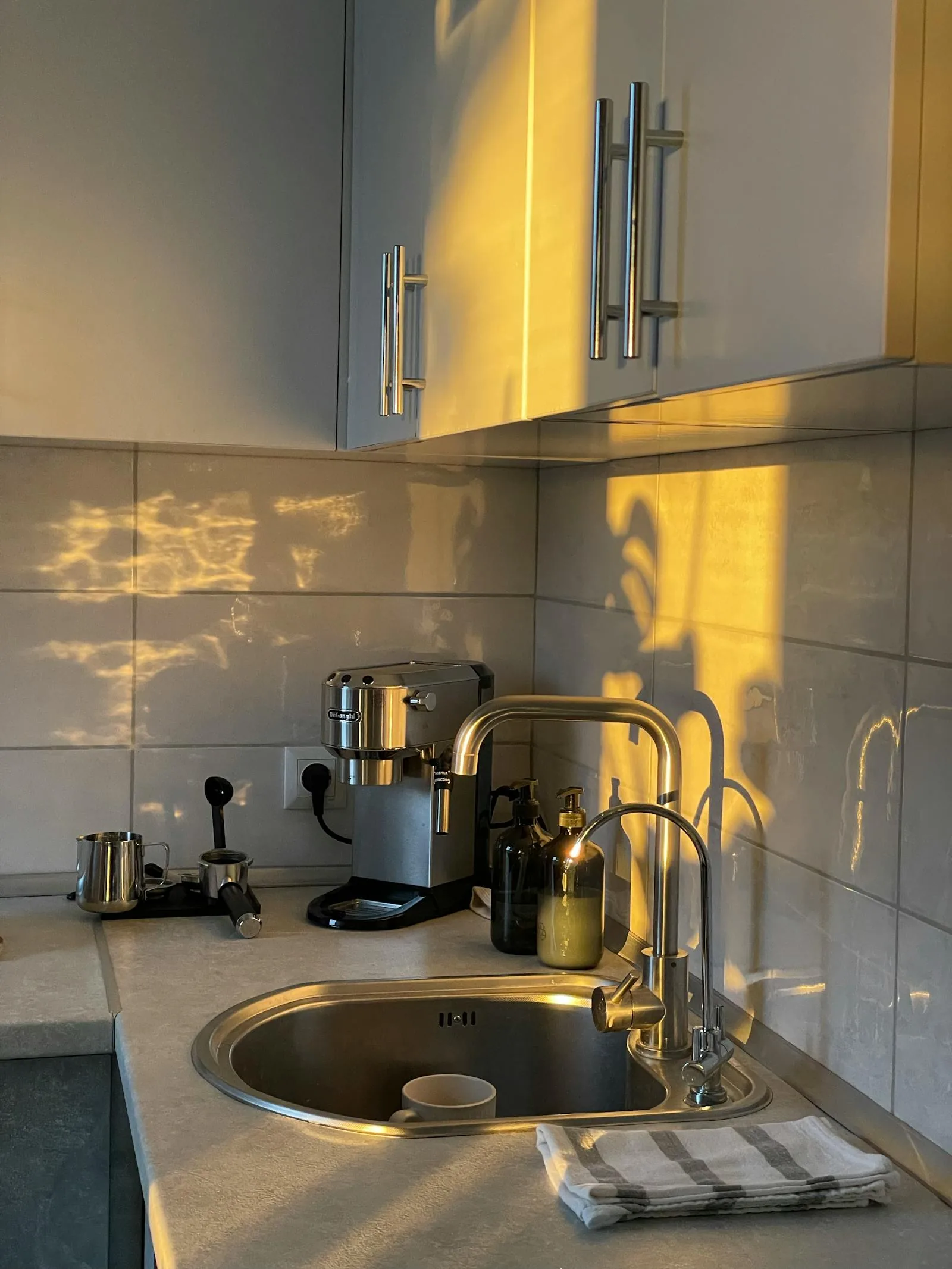 Warm kitchen counter with sink, white tile, and golden light on the working zone