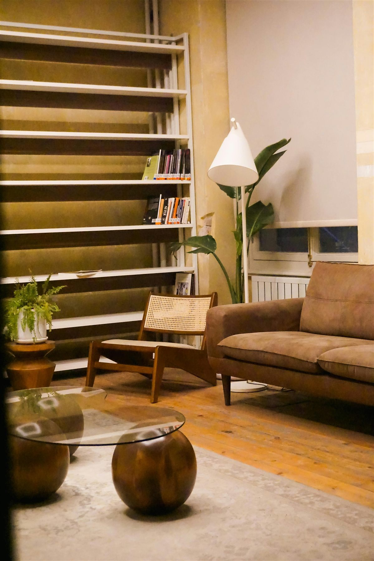 Warm room with wood shelving, tan sofa, cane chair, and softer lamp light