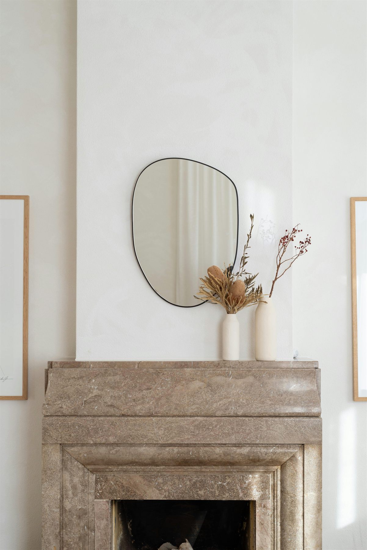 Minimal round mirror above a stone fireplace with neutral decor