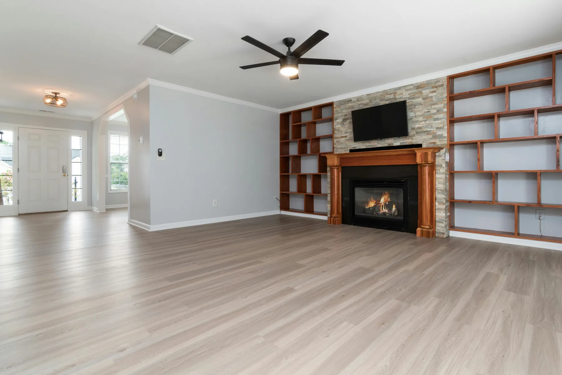 Bright empty living room with fireplace, built-in shelving, and open floor space