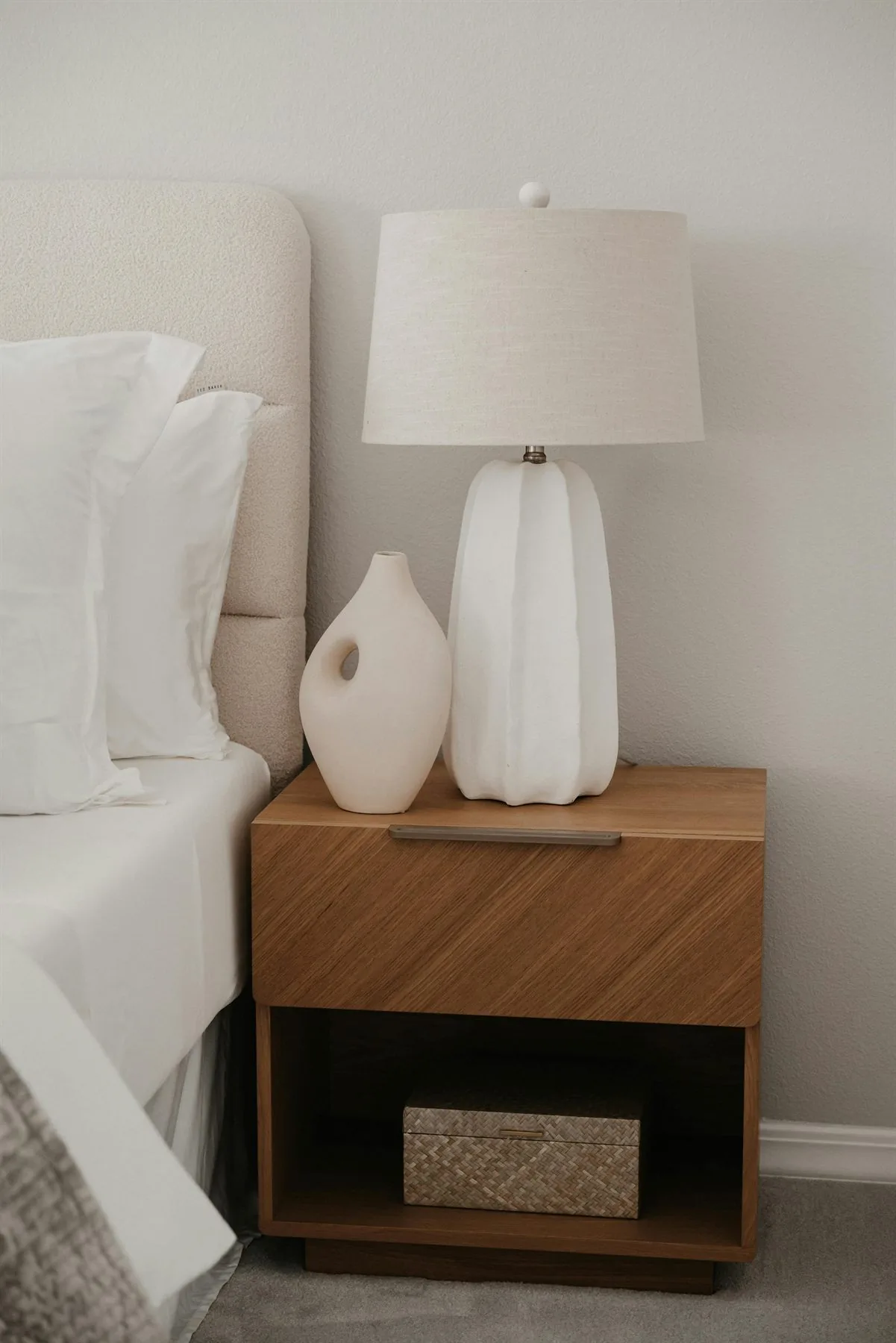 Minimal bedside table with lamp, wood drawer, and soft neutral bedding