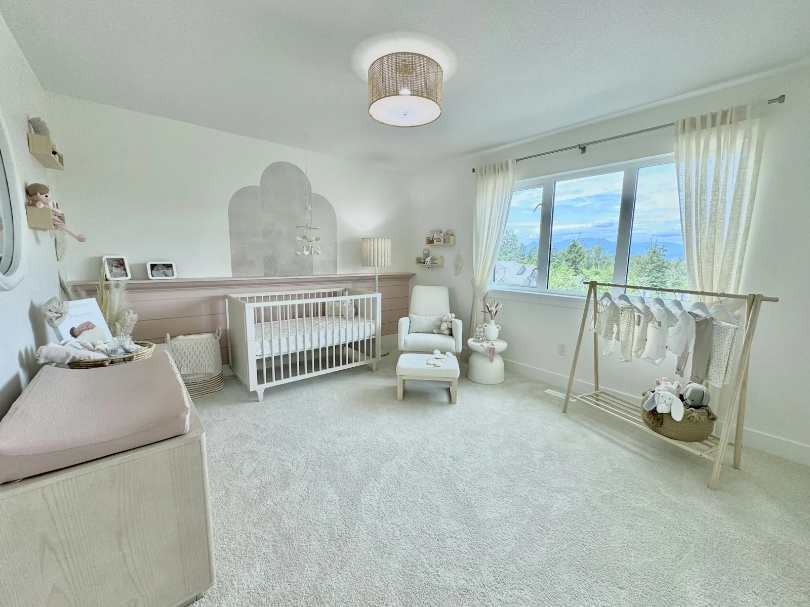 Nursery with a white crib, soft rug, light wood furniture, rocking chair, and large window
