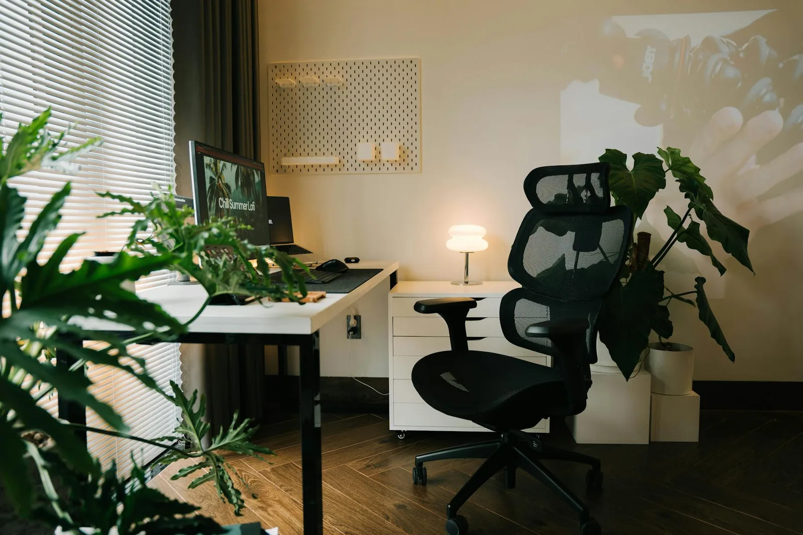 Modern office desk with ergonomic chair, plant, lamp, and soft evening light