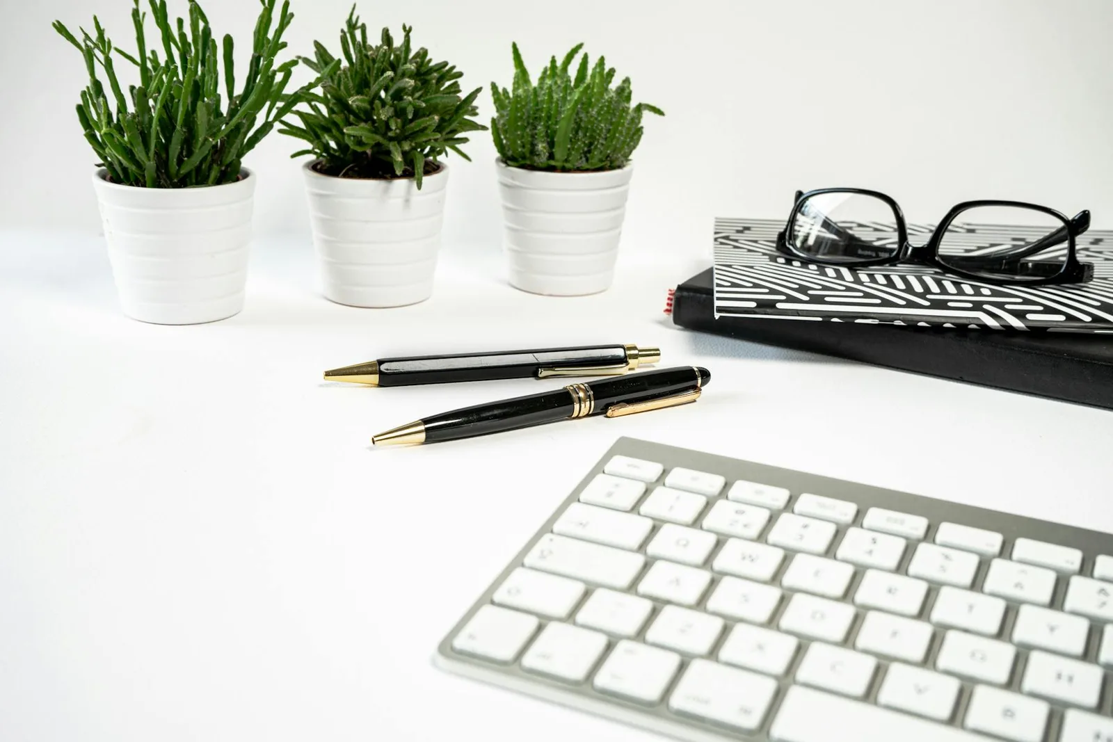 Small potted office plants beside stationery and a clean keyboard