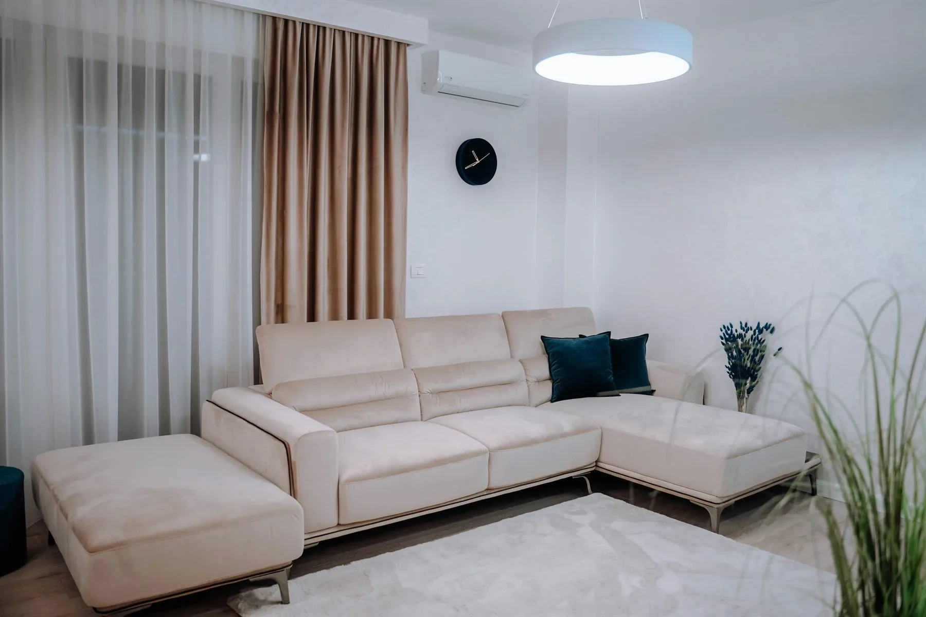Neutral living room with cream sofa, pale curtains, soft rug, and a small blue-green accent