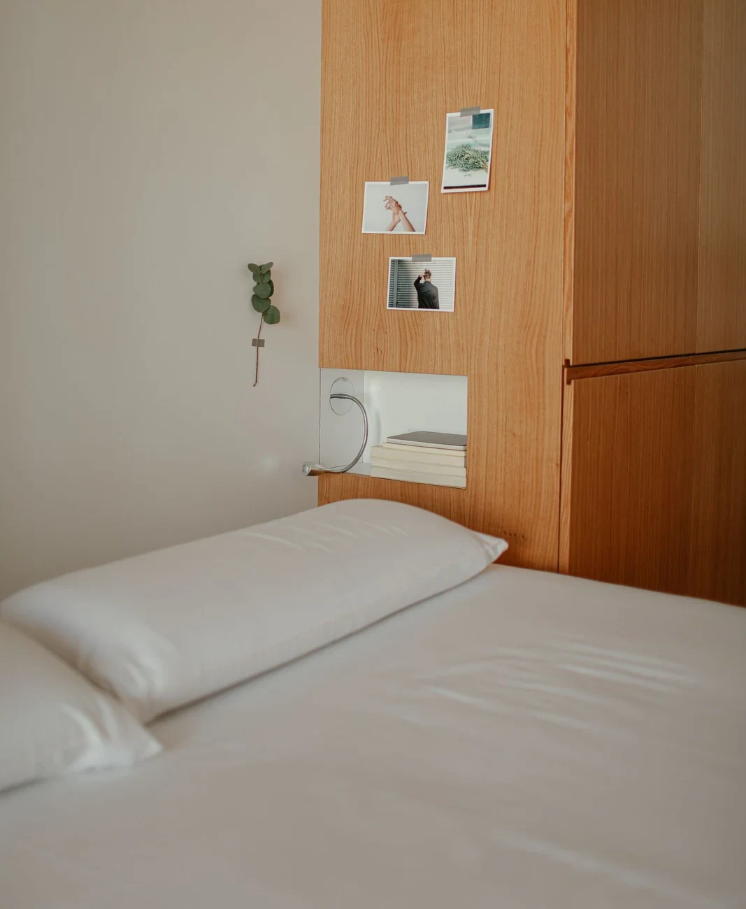 Small recessed shelf holding books and a reading light beside a bed in a timber-paneled bedroom