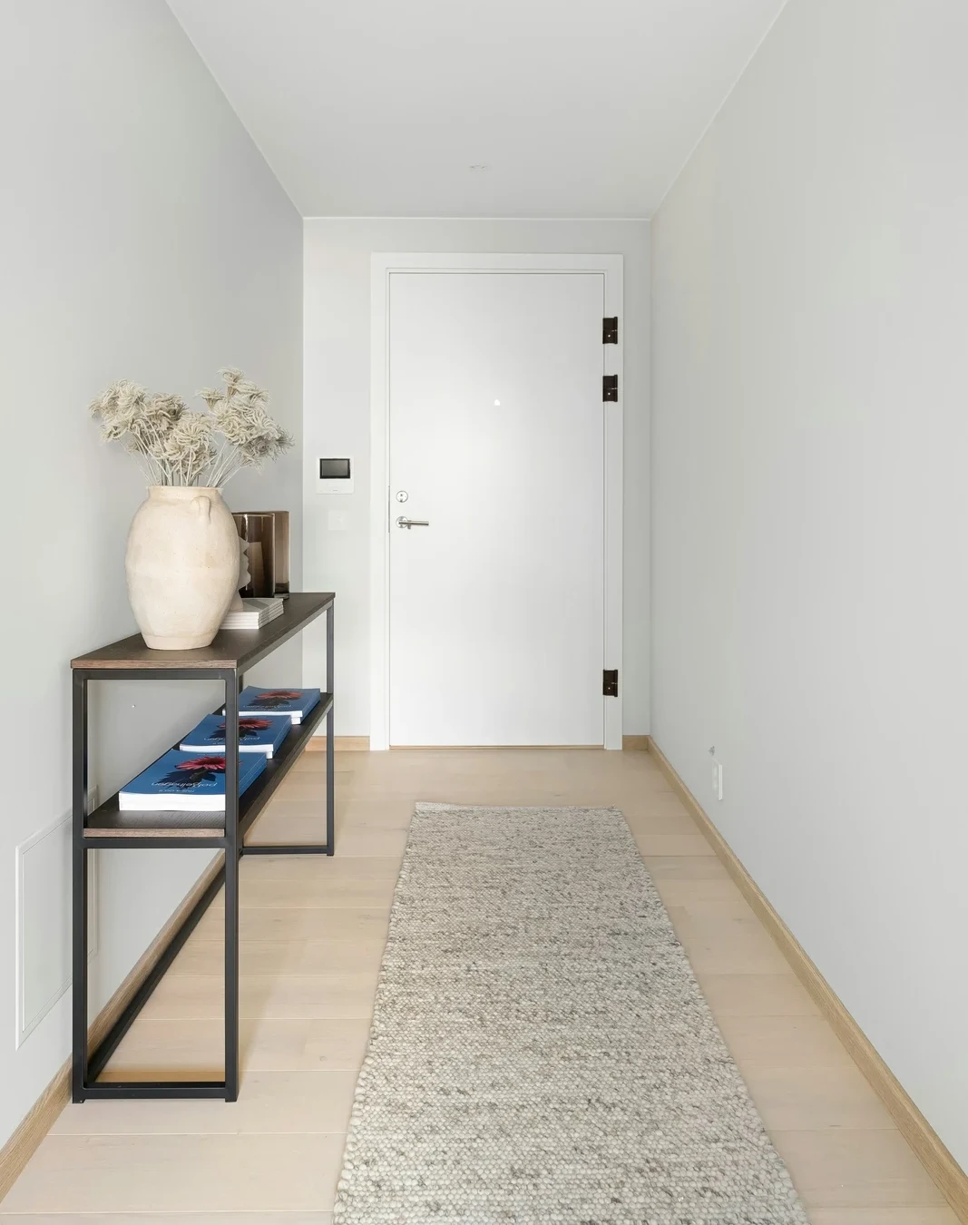 White hallway with a slim dark console along one wall, a neutral runner and a door at the end