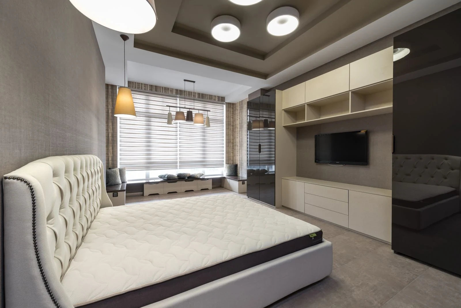 Bedroom with a wall-mounted television between pale storage cabinets opposite the bed