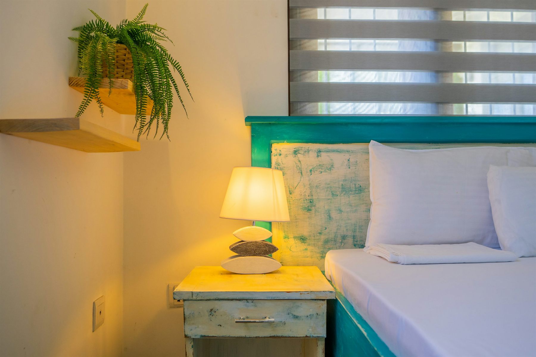 Bedroom close-up with a teal headboard, warm bedside lamp, and fern on a shelf