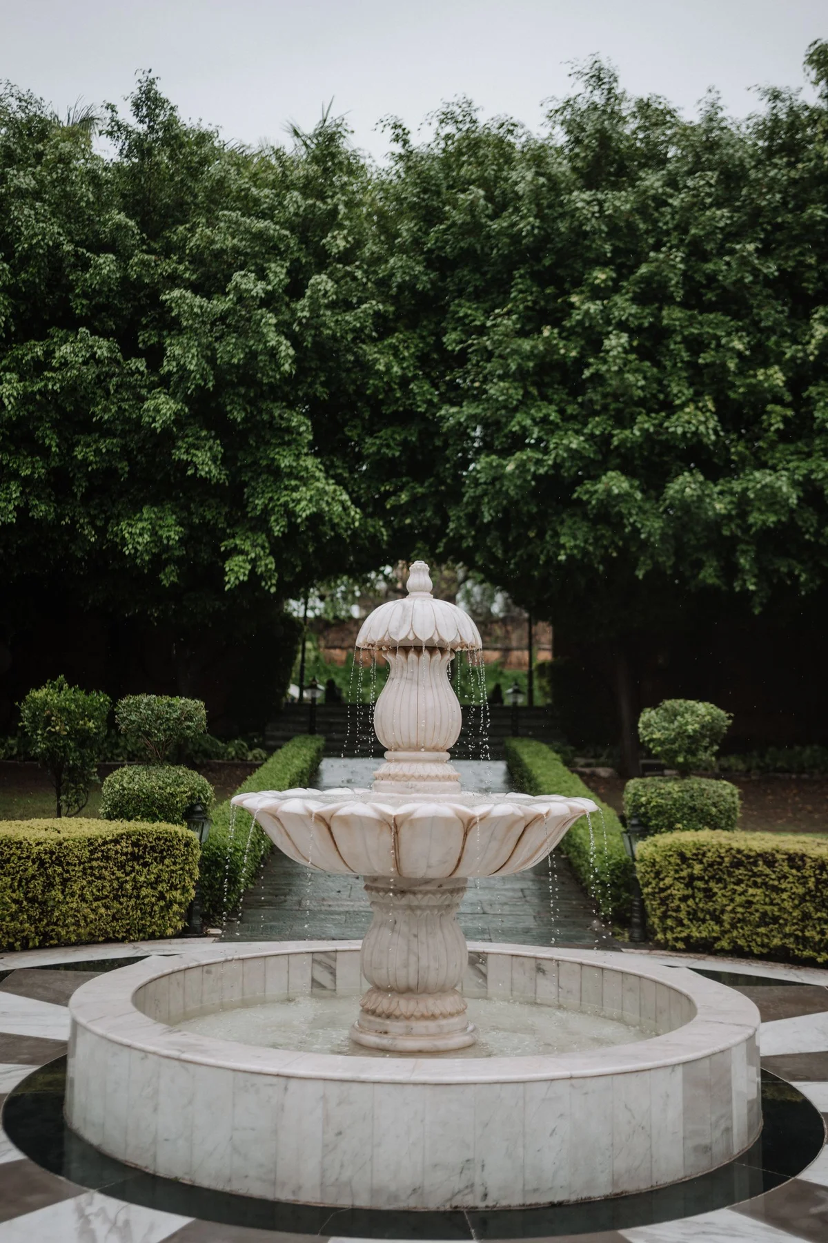 Large sculptural stone fountain and wide basin in a formal green garden