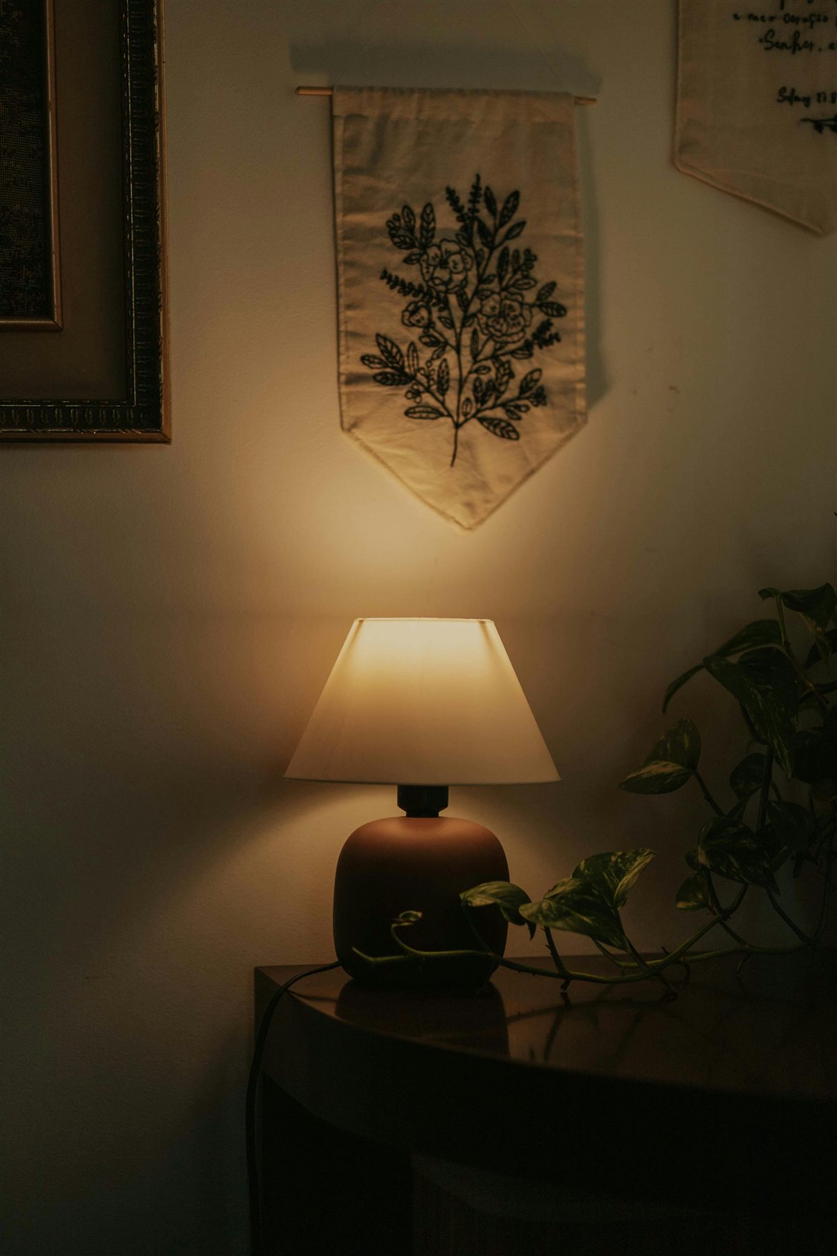 Warm lamp on a table with wall textile and plant nearby